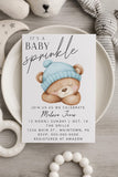 Baby sprinkle invitation with teddy bear graphic on a wooden surface with toys.